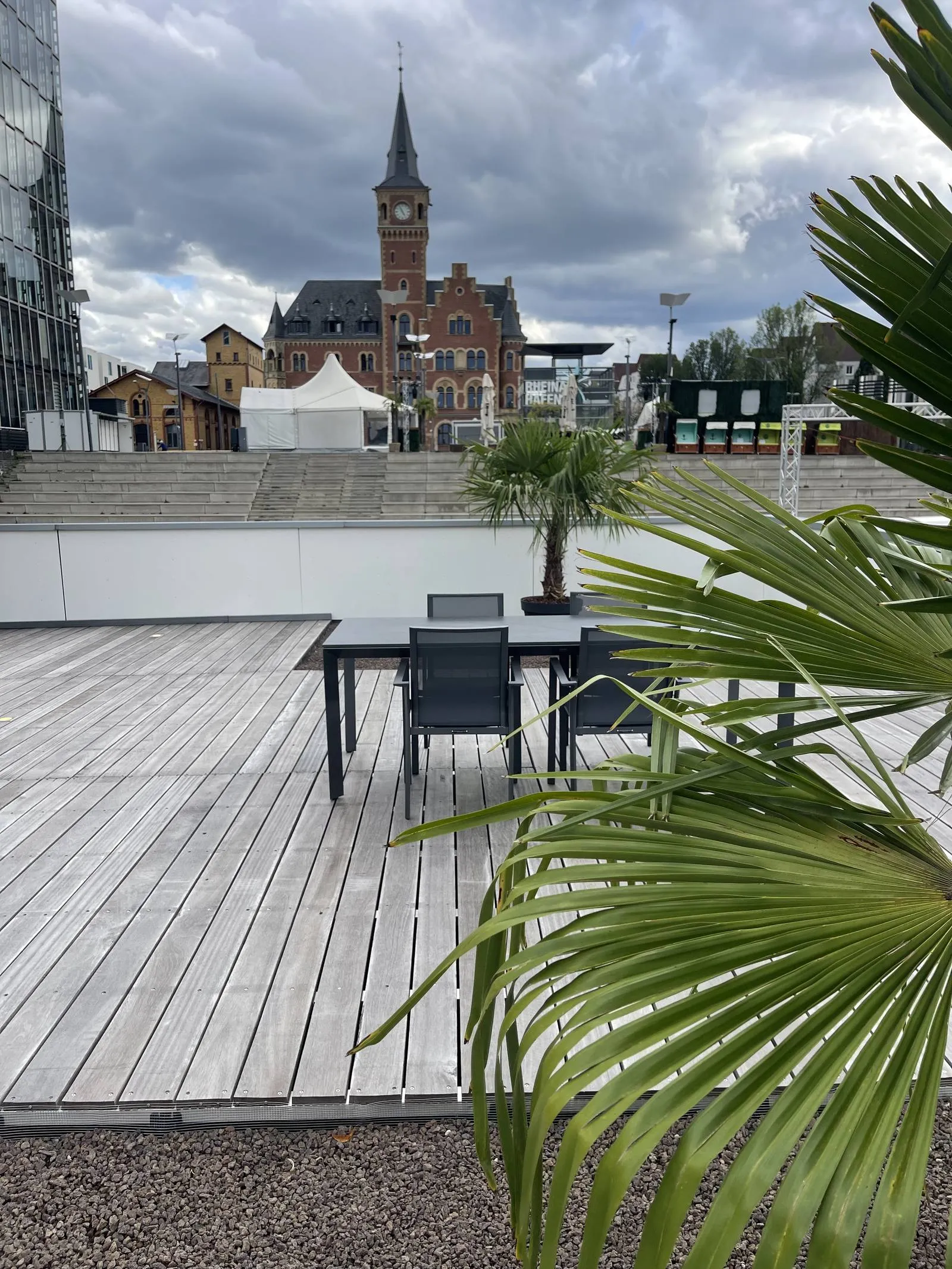 Holzterrasse der Lounge mit Esstisch und Palme, dahinter das alte Hafenamt am Rheinauhafen